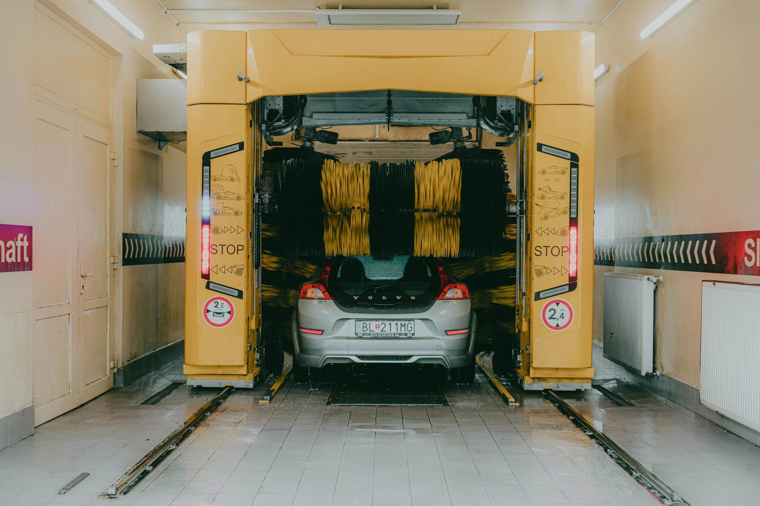 A car undergoing a cleaning process in an automated car wash station with a yellow gantry machine.
