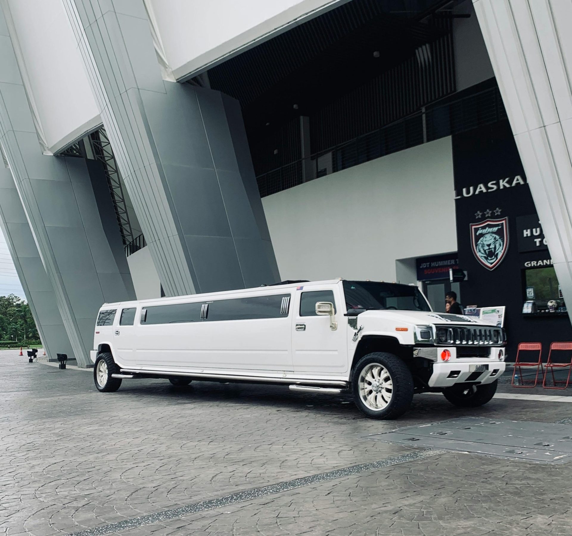 A sleek white limousine parked outside a contemporary building with geometric architecture.